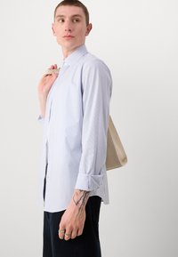 Lys blå stripete knapp-up skjorte i lett stoff med rullede ermer. Modellen holder en beige tote bag med et minimalistisk design.