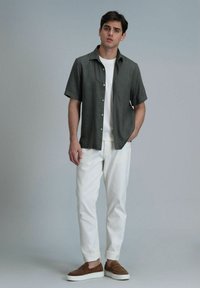 Korte mouw, knoopsluiting shirt in donkergrijze linnen, gecombineerd met witte katoenen broek en bruine suède instappers. Eenvoudig, modern ontwerp.