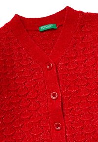 Červený pletený kardigan s texturovaným vzorem, výstřihem do V a čtyřmi červenými knoflíky. Viditelný štítek s nápisem "United Colors of Benetton".