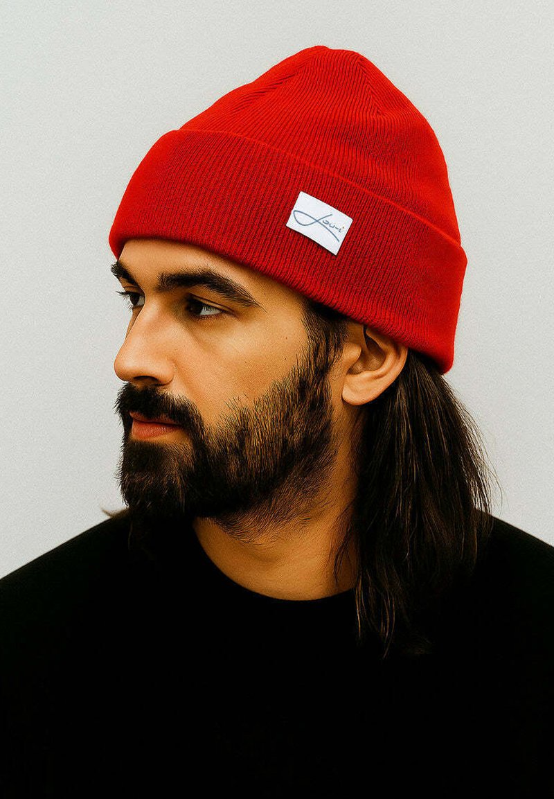 Red knitted beanie with a ribbed texture and a folded cuff, featuring a small white brand patch on the front.