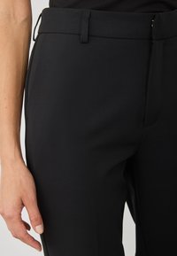 Czarne dopasowane spodnie o gładkiej fakturze, slim fit, z paskiem i kieszeniami bocznymi. Materiał wydaje się lekki i elastyczny.