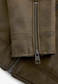 Chaqueta de cuero marrón con un primer plano de un cierre y un detalle de puño, mostrando una textura suave y sutiles acentos de cosido.