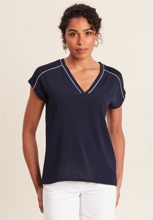 Marineblauwe T-shirt met korte mouwen en V-hals, met witte stikselaccenten, gladde textuur en een ontspannen pasvorm, gecombineerd met witte broek.