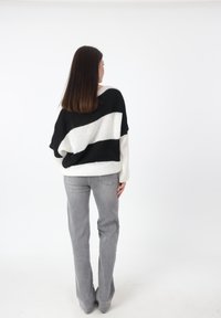 Maglione oversize a righe bianche e nere in morbido filo, indossato sopra jeans grigi chiari a zampa d'elefante, con una vestibilità rilassata e spalle basse.