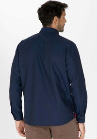 Chemise à manches longues marine avec col classique, poignets à boutons et empiècement au dos. Présente un ourlet droit et un tissu texturé.