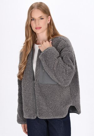 Grau-flauschige Jacke aus weichem Stoff, mit einem Reißverschlussverschluss und einer einfarbigen grauen Tasche auf der Brust. Texturierte und übergroße Form.