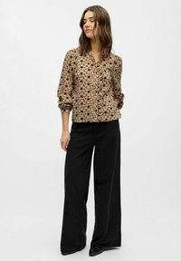 Blusa marrón de flores con botones, de manga larga y puños fruncidos, combinada con pantalones anchos negros y zapatos negros de punta. Textura de tela suave.