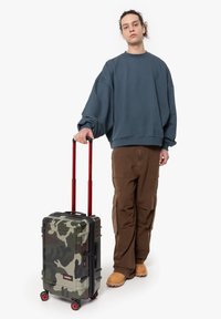 Svart och grön kamouflage hårdskaligt resväska med röd teleskophandtag och hjul, utrustad med en sidokonsol och dragkedjestängning.