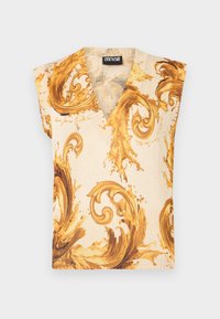 Haut beige sans manches avec un profond décolleté en V, présentant de grands motifs baroques ornés de volutes en brun doré et une étiquette noire au col.