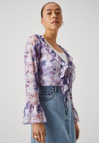 Sheer, purple floral blouse with ruffled neckline and bell sleeves, paired with a light blue denim skirt. Textured fabric, delicate pattern.