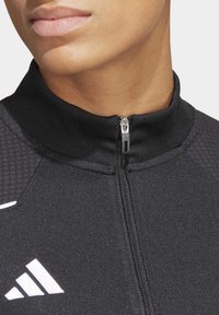 Giacca atletica nera con colletto zip, tessuto testurizzato e dettagli in bianco sul logo davanti, che mostra un primo piano del collo.