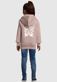 Lyserød hettegenser med ryggtrykk som har en hvit sommerfugl og teksten "COOL KARMA." Kombinert med blå denimjeans og svarte joggesko.