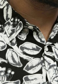 Schwarz kurzärmliges Hemd mit weißem Blumenmuster. Verfügt über einen Button-Down-Kragen und einen weichen, strukturierten Stoff.