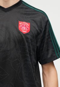 Μαύρη αθλητική φανέλα με διακριτικό λουλουδένιο σχέδιο, πράσινες ρίγες στα μανίκια και κόκκινο έμβλημα All-Stars 1994 στο στήθος.