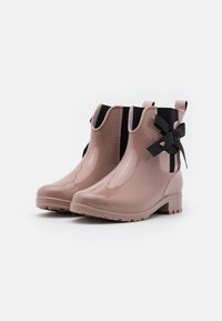 Bottes de cheville en caoutchouc rose brillant, avec un faible talon, présentant un panneau élastique noir et un accent en nœud sur le côté. Semelle texturée pour une meilleure adhérence.