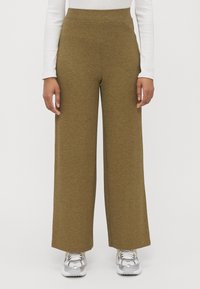 Olive green ribbed wide-leg pants with a high waist, made of soft fabric. Paired with shiny silver sneakers and a white long-sleeve top.