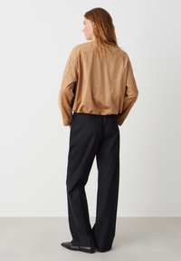 Camicia oversize in suede marrone con spalle scese, abbinata a pantaloni neri a gamba larga. Texture liscia con dettagli di cucitura minimi.