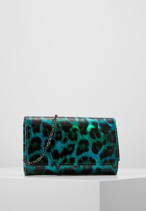 Pochette rectangulaire brillante avec motif léopard bleu et vert et une chaîne en argent, posée sur un piédestal blanc.