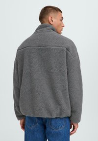 Gray fleece jacket with a high collar, textured fabric, and relaxed fit. Features dropped shoulders and a straight hem.