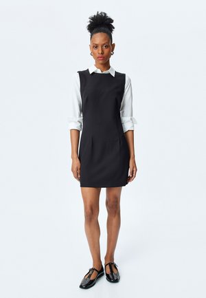 Schwarzes ärmelloses Kleid mit Rundhalsausschnitt, kombiniert mit einem weißen Hemd mit Kragen. Glatter Stoff, minimalistisches Design und knielang.
