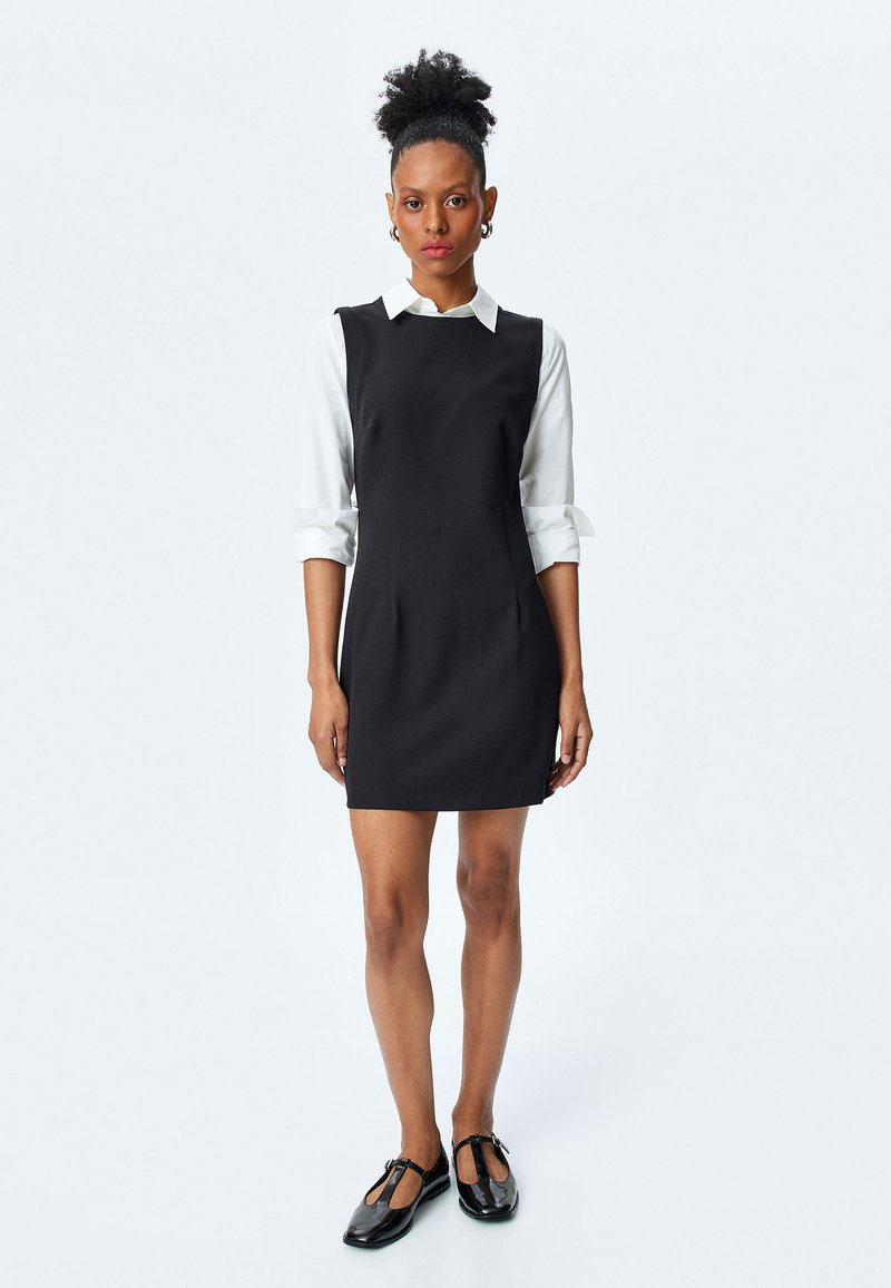Schwarzes ärmelloses Kleid mit Rundhalsausschnitt, kombiniert mit einem weißen Hemd mit Kragen. Glatter Stoff, minimalistisches Design und knielang.