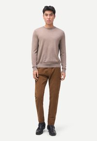 Beiger Strickpullover mit Rundhalsausschnitt, kombiniert mit brauner Cordhose und schwarzen Lederstiefeln, mit strukturierter Oberfläche und legerer Passform.