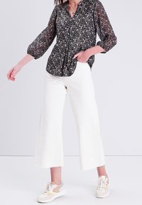 Blouse florale noire avec des manches longues froncées et un col en V, assortie à un jean large blanc et des baskets beiges. Tissu texturé.
