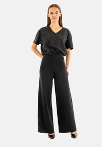 Top a V con pois neri abbinato a pantaloni neri a gamba larga con vita alta. Tessuto morbido con una vestibilità comoda e un leggero lucido.