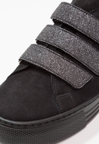 Basket noire avec trois bandes velcro argentées brillantes et semelle épaisse en caoutchouc texturé.