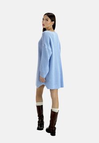 Abito maglione oversized azzurro con maniche lunghe e spacchi laterali, abbinato a stivali marroni fino al ginocchio e gambaletti color crema.
