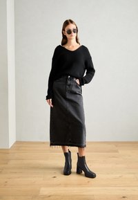 Pull noir côtelé avec un décolleté en V, associé à une jupe en denim noir taille haute avec un ourlet effiloché, et des bottines noires à talons.