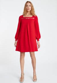 Rotes Kleid mit langen, gepufften Ärmeln, quadratischem Ausschnitt und einem dekorativen goldenen Akzent. Hergestellt aus einem glatten, leichten Stoff mit einer ausgestellten Silhouette.