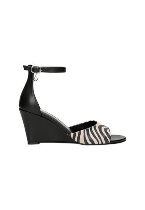 Sandali con tacco a cuneo con un cinturino alla caviglia in pelle nera e una parte anteriore con stampa zebra color tan. Presentano un tacco a cuneo elegante e curvato per un'altezza extra.