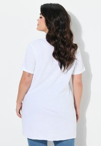 Camiseta de algodón blanca de manga corta, con un diseño de parte trasera más larga. Textura suave, estilo minimalista y sin patrones ni herrajes visibles.