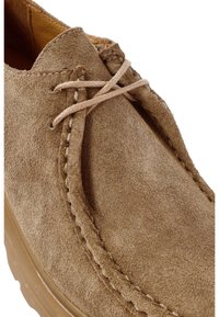 Zapato de ante marrón con punta redonda, detalles de costura y cordones planos; presenta una superficie texturizada y una suela de goma ligera.