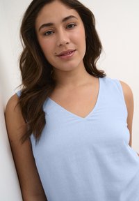 Haut sans manches de couleur bleu clair avec un décolleté en V. Fabriqué à partir d'un tissu doux et texturé. Apparence simple et minimaliste.