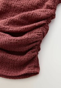 Getextureerde stof in een rijke bordeauxkleur, met zachte plooien en een geraffineerd detail, dat een gezellige, gebreide uitstraling heeft.