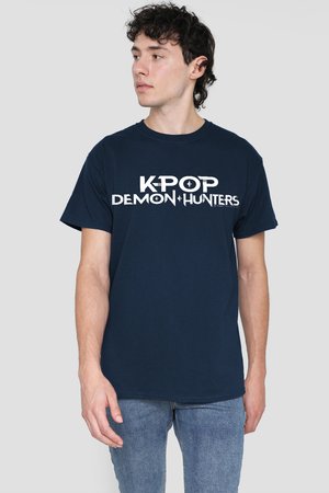Junger Mann mit dunklem lockigem Haar, der ein marineblaues T-Shirt mit weißer Aufschrift "K-POP DEMON HUNTERS" trägt und nach links schaut, vor einem einfarbigen Hintergrund.
