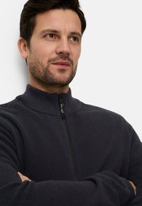 Dunkelgrauer Reißverschluss-Pullover mit hohem Kragen, gerippter Textur und eng anliegendem Schnitt. Verfügt über einen kontrastierenden Reißverschluss und strukturierter Stoff.