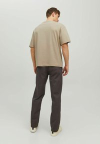 Camicia beige a maniche corte con una vestibilità rilassata, abbinata a pantaloni grigi scuri. L'outfit presenta un design semplice e una texture del tessuto morbida.