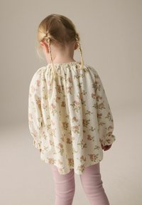 Weiße Bluse mit Blumenmuster, gepufften Ärmeln, gerafftem Ausschnitt und hellrosa Blumen. Kombiniert mit hellrosa Leggings. Strukturierter Stoff.