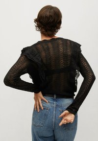 Mustat pitsineuleet, joissa on rypytetyt olkapäät, ja neuleessa on teksturoitu kuvio ja tiukat hihat. Yhdistetty korkeavyötäröisiin farkkuihin.