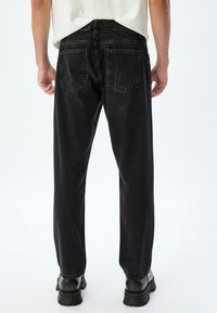 Jeans de mezclilla negra con corte recto, que cuentan con bolsillos traseros y un desgaste mínimo. Combinados con botas negras de suela gruesa, el conjunto tiene un diseño moderno.