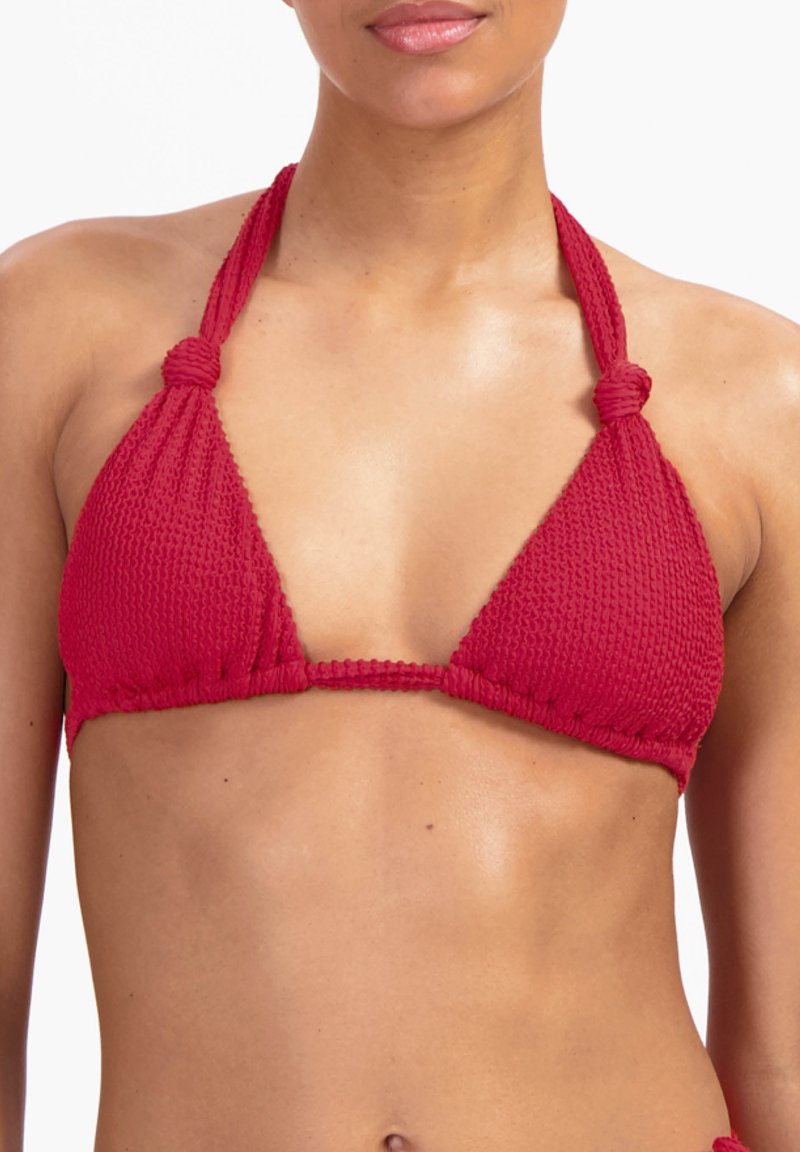 Femme portant un haut de bikini rouge texturé avec des bretelles nouées en tour de cou, vue des épaules jusqu'au milieu du ventre sur fond blanc.