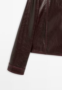 Giacca in pelle bordeaux con una texture liscia, caratterizzata da un design strutturato, maniche lunghe e dettagli finemente cuciti sui polsini.
