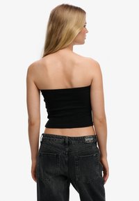 Top negro sin tirantes hecho de material elástico, diseño ajustado. Combinado con jeans de talle alto en gris oscuro, con bolsillos traseros y etiqueta.