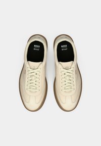 Kreemivärvi nahast tennised ümarate varvastega, paeltega ja pruuni kummist tallaga. Omavad keelel logot ja polsterdatud sisetald.