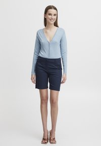 Gilet v-neck bleu clair avec fermeture à boutons, associé à un short noir marine bien ajusté. Tissu lisse avec un design ajusté et une longueur mi-cuisse.
