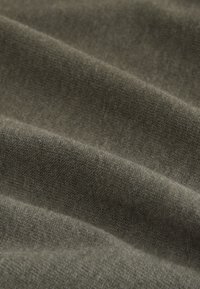 Nahaufnahme von weichem, olivgrünem Strickstoff mit feiner Textur und dezenten Falten.