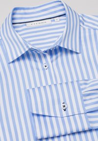 Camicia a righe blu chiaro e bianca con colletto pieghevole, chiusura con bottoni e taschino sul petto. Realizzata in tessuto morbido con una finitura fresca.